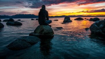 person sitting on rock on body of water